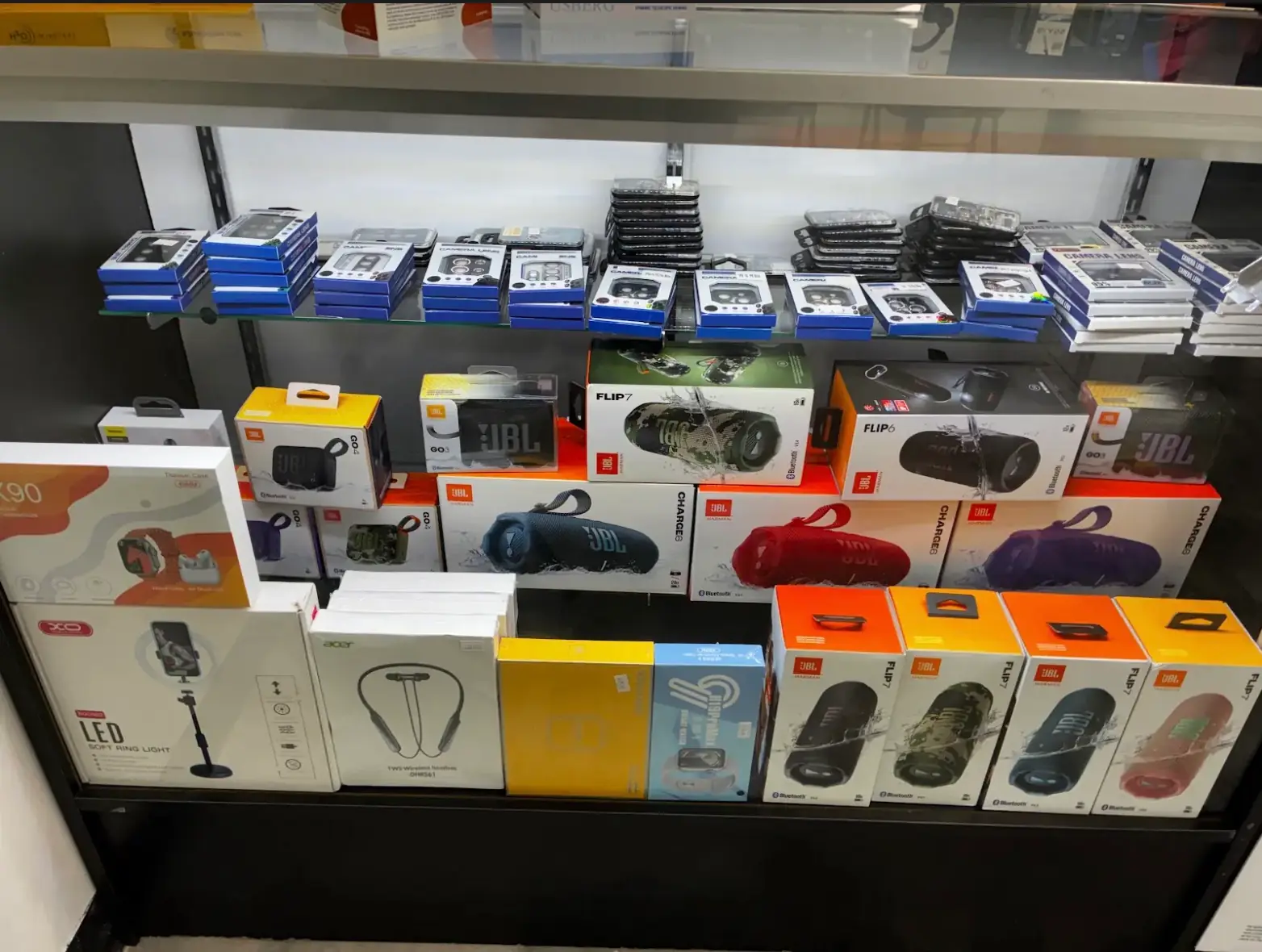 Bocinas JBL Flip 7, Charge 6 y Go 4 y protectores de cámara en la vitrina